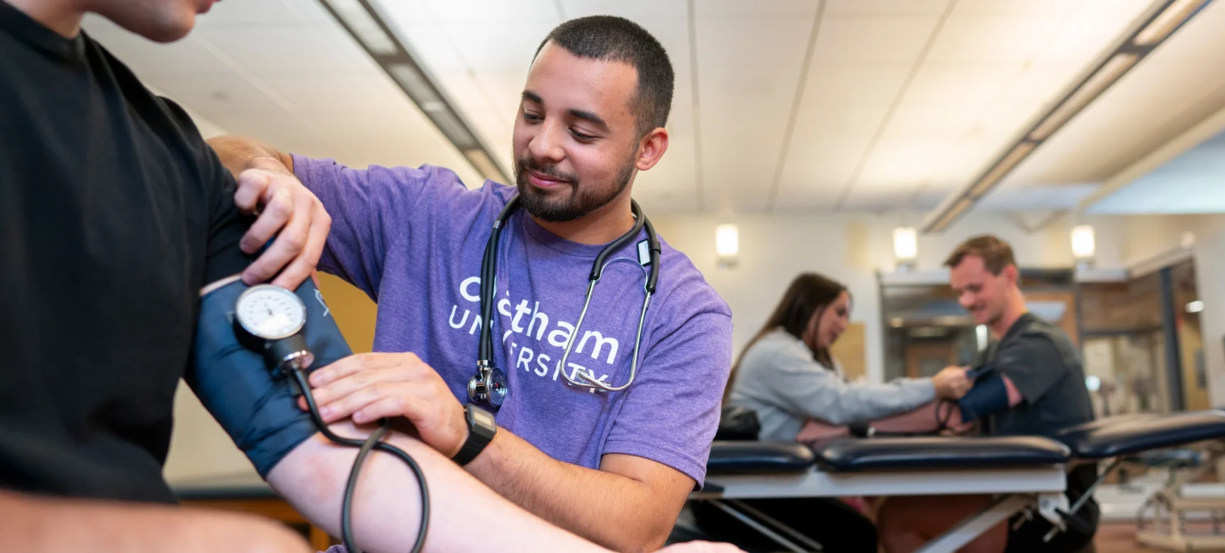 Student in a Chatham University shirt using a blood pressure cuff to check another student’s arm
